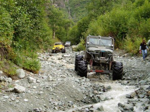 2000 Ford E350 - Multiple off-road vehicles navigate a challenging, rocky stream bed in a wooded area.