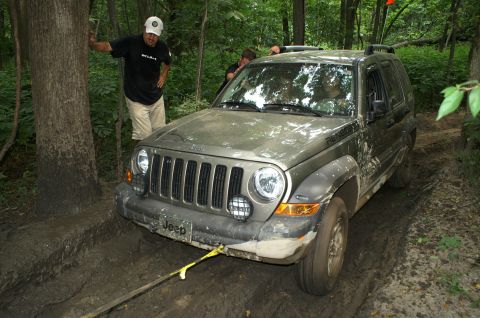 2006 Jeep Liberty - A Jeep Liberty is stuck in the mud on a wooded trail, with two people attempting to assist.