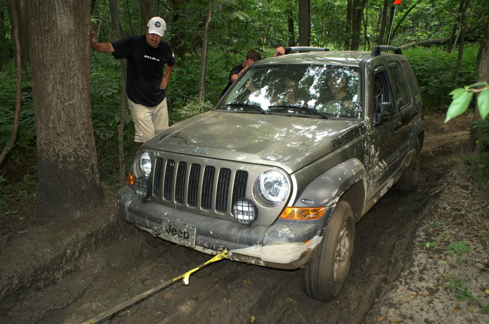 2006 Jeep Liberty stuck in mud on a wooded trail, with two people nearby