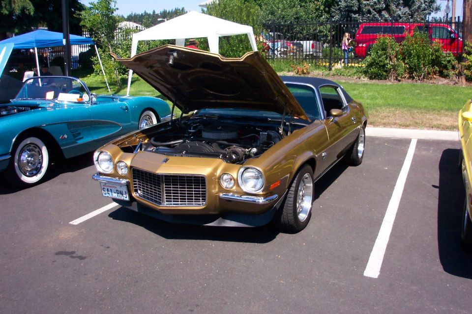Gold 1970 Chevrolet Camaro parked with hood open, next to a blue convertible