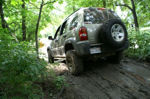 2006 Jeep Liberty - A Jeep Liberty navigates a challenging muddy incline surrounded by dense foliage.