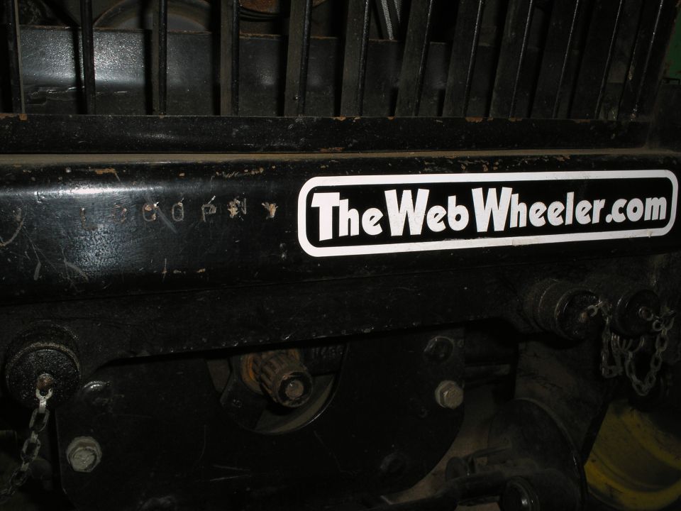 Close-up of a black metal part on a tractor with a sticker that says TheWebWheeler.com