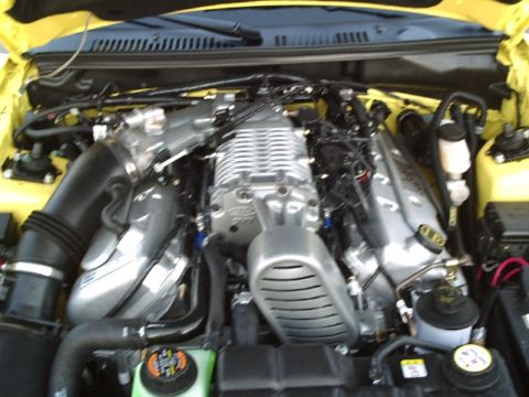 1989 Ford Mustang - The engine bay of a yellow car, showing a prominent supercharger and various engine components.