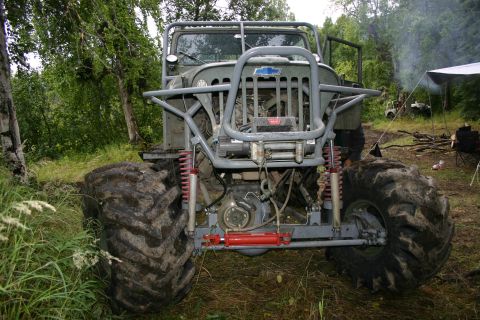 2003 Jeep TJ - A heavily modified off-road vehicle sits in a campsite clearing, with smoke rising in the background.