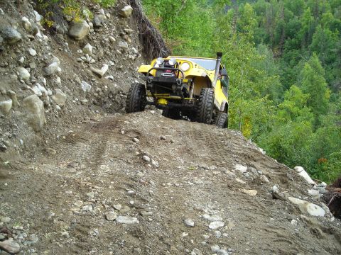 2003 Jeep TJ - A yellow Jeep navigates a steep, off-road trail covered in rocks and mud.