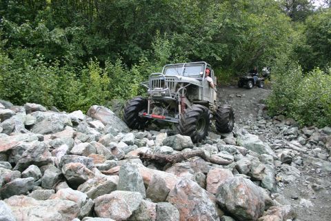2003 Jeep TJ - A heavily modified off-road vehicle with oversized tires tackles a challenging rocky terrain, with another ATV visible in the background.