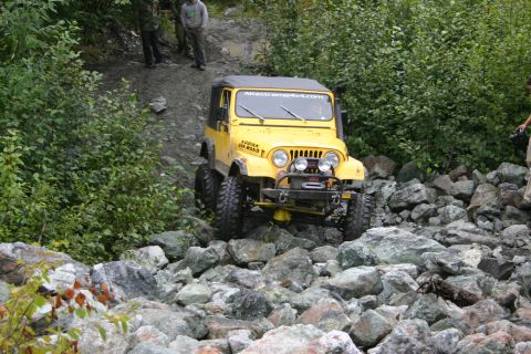 2003 Jeep TJ - A yellow Jeep Wrangler TJ tackles a challenging rocky terrain, with "AKEXTREME4X4.COM" visible on its windshield banner.