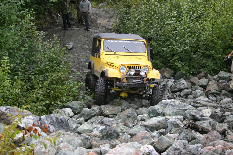 Yellow Jeep Wrangler TJ navigating a rocky trail with "AKEXTREME4X4.COM" on windshield banner