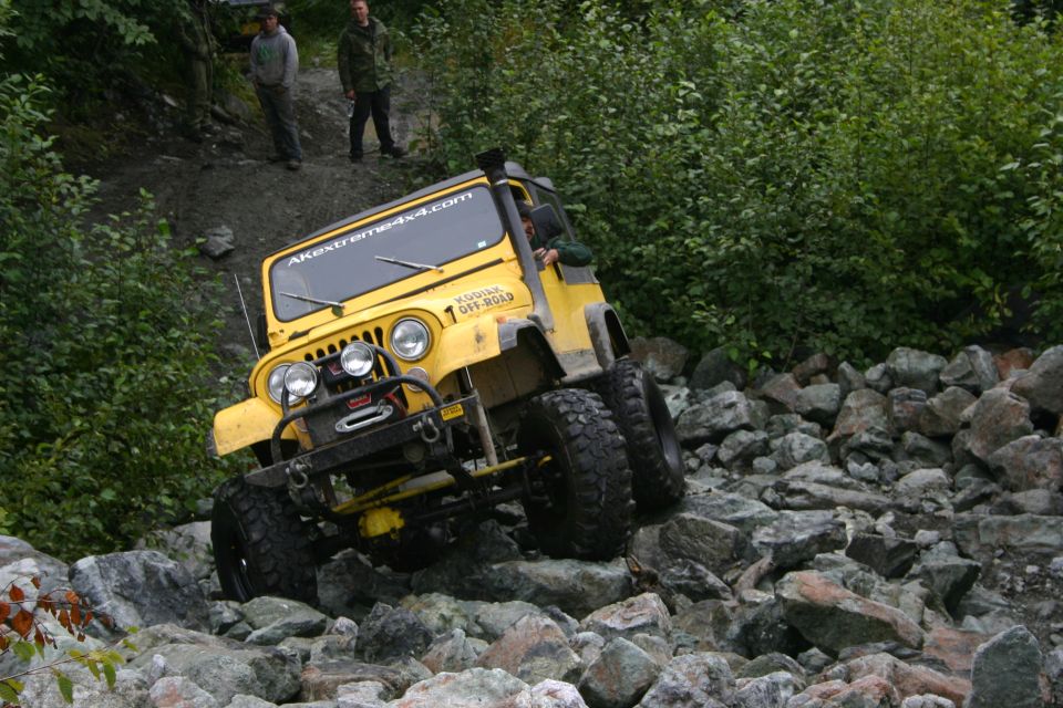 Yellow Jeep CJ with off-road tires navigating a rocky trail. AKextreme4x4.com sticker on windshield