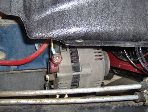 1978 Ford Bronco - Engine bay close-up of an alternator mounted low on a blue-painted engine block, with a heavy red charging cable and a yellow exciter wire…
