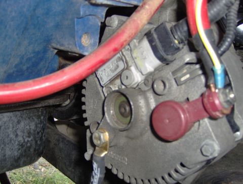 1978 Ford Bronco - Tight shot of a cast-aluminum Motorcraft alternator rear housing with its finned case, brass ground bolt, red insulated output terminal boo…