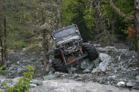 2003 Jeep TJ - A heavily modified Jeep navigates a challenging rocky stream bed in a wooded area.