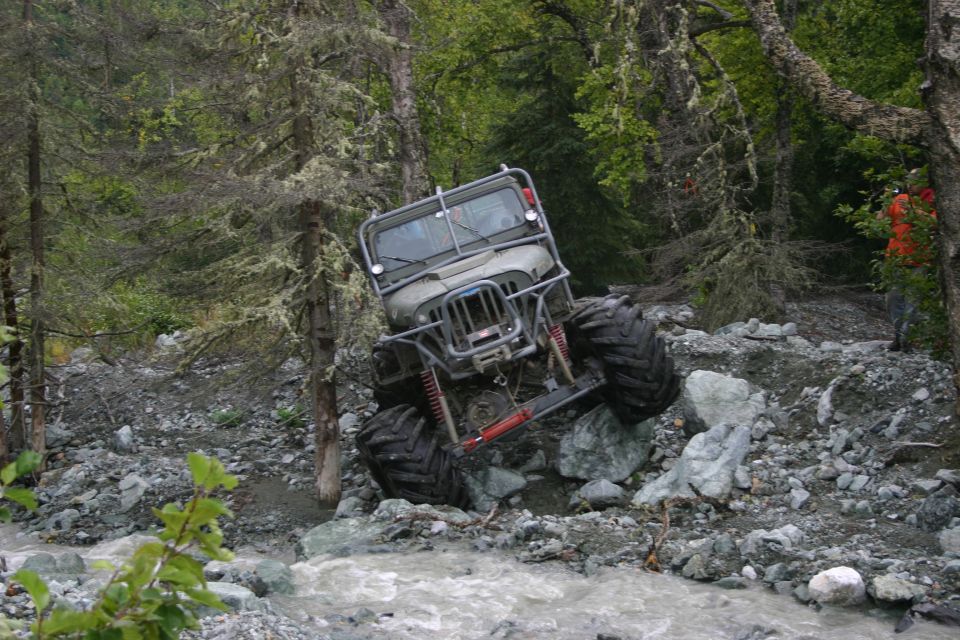 Modified Jeep with large tires navigating rocky terrain next to a stream