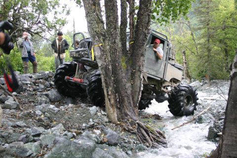 2003 Jeep TJ - An extreme off-road vehicle maneuvers through a shallow, rocky stream in a wooded area.