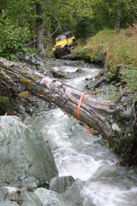 2003 Jeep TJ - A yellow 2003 Jeep TJ navigates a challenging off-road course through a shallow stream.