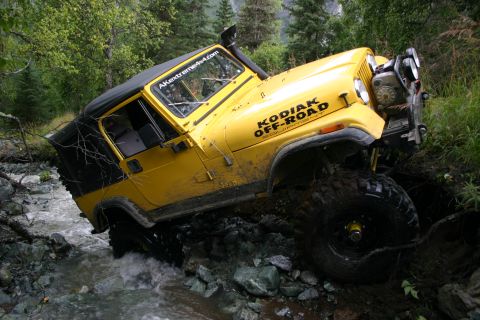 2003 Jeep TJ - A yellow Jeep TJ is shown off-roading through a rocky stream, with "KODIAK OFF-ROAD" visible on its side.