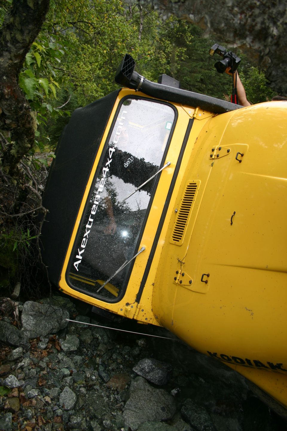 Yellow off-road vehicle tipped over on rocky terrain with a snorkel. Text on window reads Akextreme4x4.com