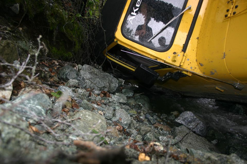 Yellow vehicle partially submerged in water and rocks, with text 'AKROKS' visible on the window