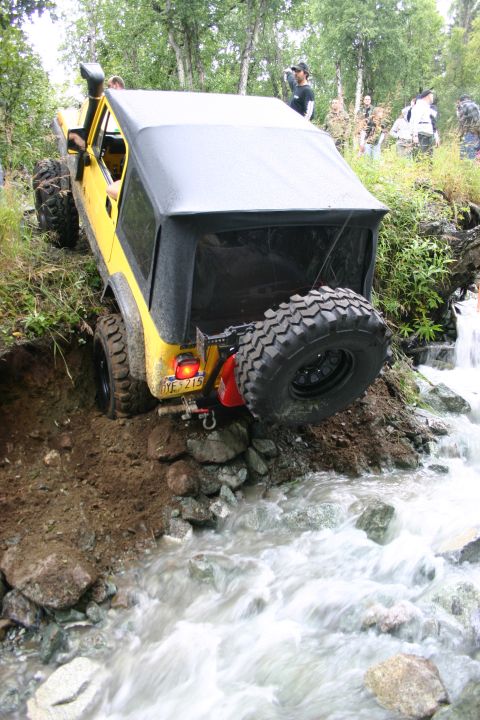 2003 Jeep TJ - A yellow Jeep TJ navigates a challenging off-road course, descending into a rocky stream.