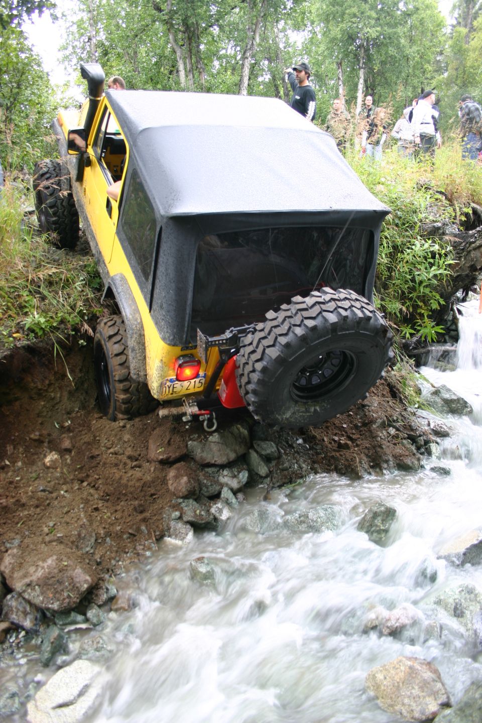 Yellow Jeep TJ going down a rocky stream bank, spare tire on back