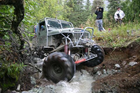 2003 Jeep TJ - A heavily modified Jeep Wrangler with oversized tires tackles a challenging rocky stream during an off-road excursion.