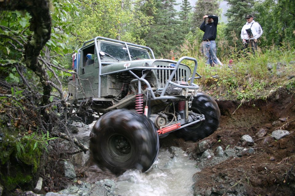Modified Jeep Wrangler navigating a rocky stream with large tires