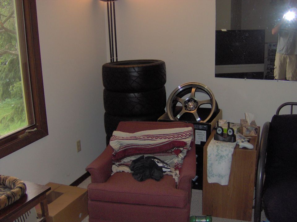 Silver five-spoke car wheel and stack of black tires in a room