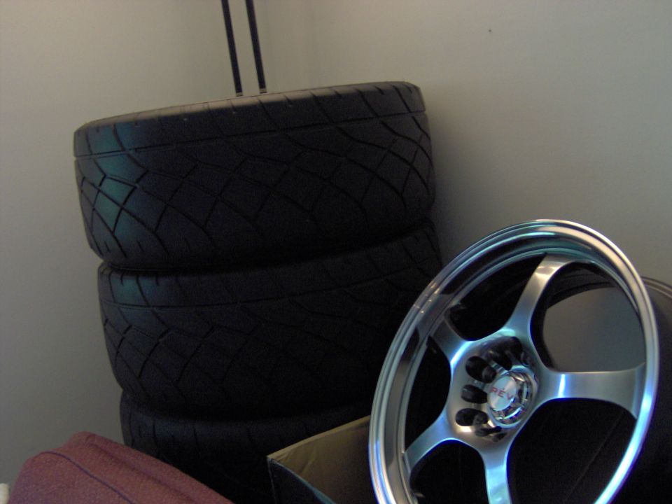 Stack of three tires next to a silver 5-spoke aftermarket wheel