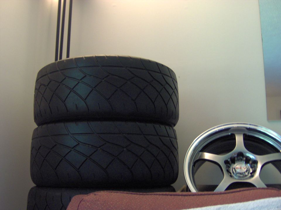 Two tires stacked on top of each other next to a silver five-spoke car wheel