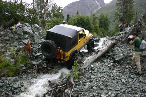 2003 Jeep TJ - A yellow Jeep Wrangler navigates a challenging off-road path through a rocky stream.