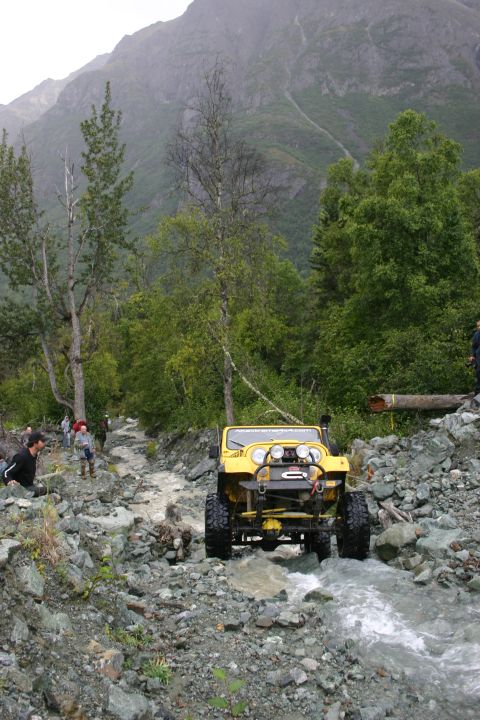 2003 Jeep TJ - A yellow Jeep Wrangler navigates a challenging rocky stream bed in a mountainous, wooded area.