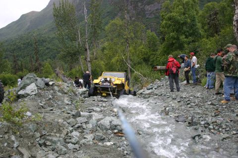 2003 Jeep TJ - A group of people assist in winching a yellow Jeep TJ out of a rocky stream bed in a wooded area.