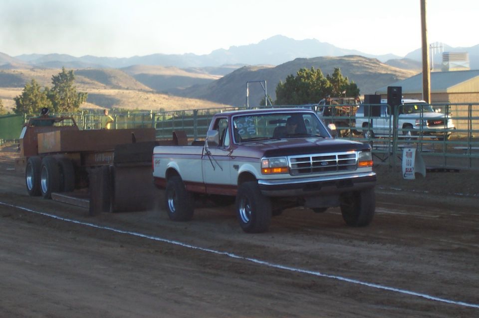 Ford pickup truck pulling a sled on a dirt track, mountains in background