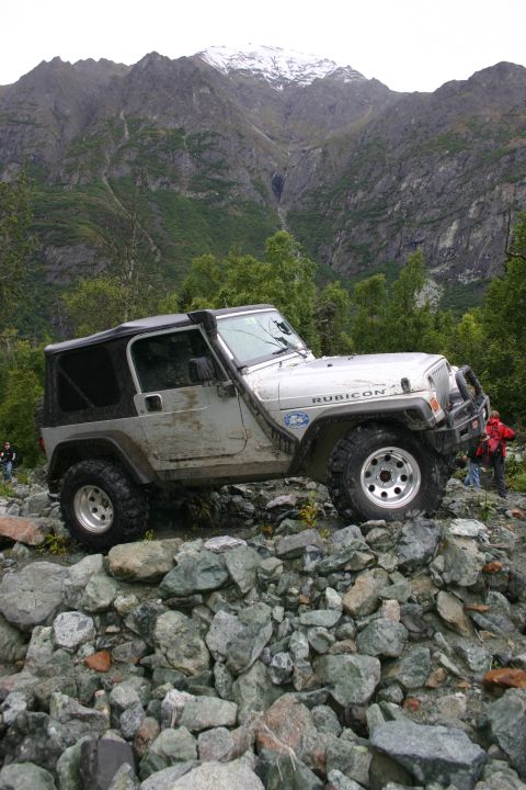 2003 Jeep TJ - A silver Jeep Wrangler TJ Rubicon navigates a rocky trail with a snow-capped mountain in the background.