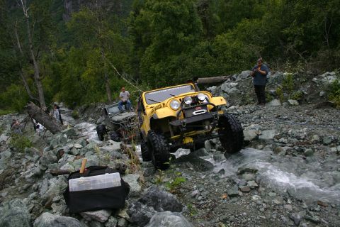 2003 Jeep TJ - Two modified Jeeps navigate a challenging rocky stream bed in a wooded mountain area.