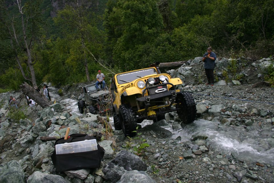 Yellow Jeep Wrangler driving through rocky stream, another Jeep behind it