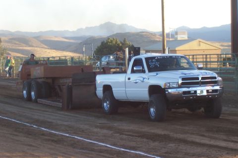 1994 Ford F-150 - A white pickup truck competes in a pulling event, dragging a heavy trailer across a dirt track.