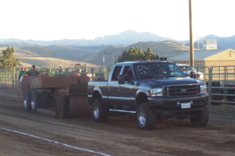 1994 Ford F-150 - A dark blue pickup truck tows a trailer across a dirt track, with mountains in the background.