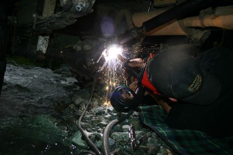 2003 Jeep TJ - Welding repairs being performed on a vehicle's exhaust system in an outdoor, rocky environment.
