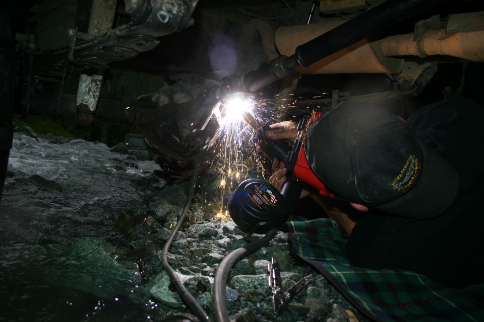 Person welding exhaust pipe under a vehicle near a rocky stream