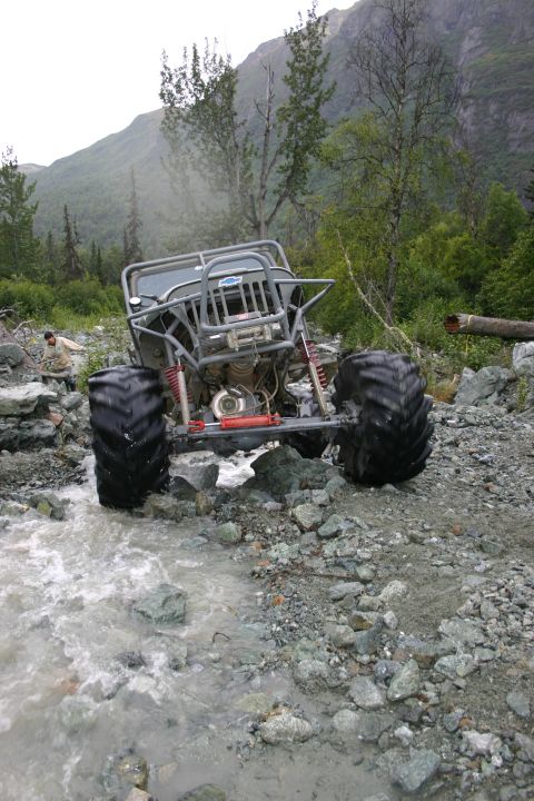 2003 Jeep TJ - An off-road vehicle with oversized tires navigates a rocky stream bed in a mountainous, wooded area.