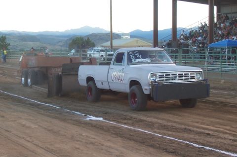 1994 Ford F-150 - A pickup truck competes in a pull event, dragging a heavy trailer across a dirt track.