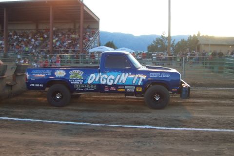 1994 Ford F-150 - A blue pickup truck, branded "DIGGIN' IT", competes in a truck pull event with spectators in the background.