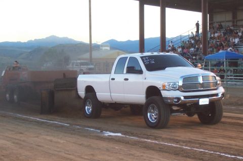 1994 Ford F-150 - A white Dodge Ram pickup truck competes in a truck pull event, dragging a weighted sled across a dirt track.