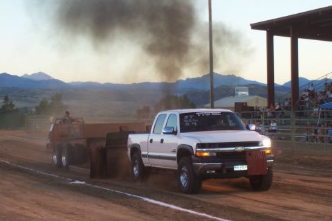 1994 Ford F-150 - A white pickup truck emits black smoke while pulling a heavy trailer in a competition.