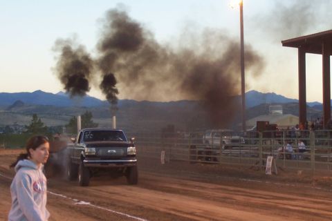 1994 Ford F-150 - A truck competes in a pull event, kicking up dust and smoke under a clear sky with mountains in the distance.