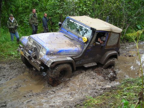 2003 Jeep TJ - Blue Jeep TJ deep in mud on an off-road trail with people watching.
