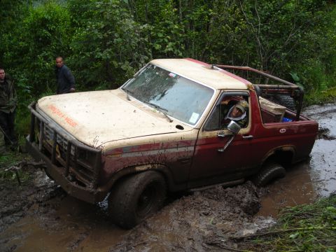 2003 Jeep TJ - This off-road vehicle is deeply stuck in a muddy trail surrounded by dense foliage.