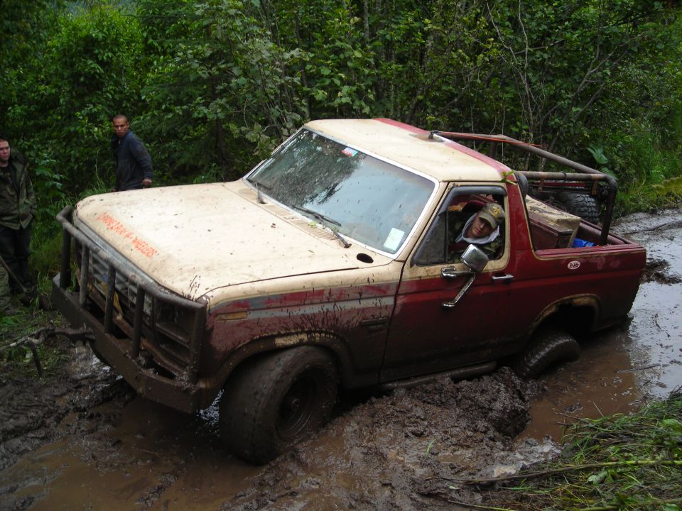 Ford Bronco stuck in mud with driver inside. Two people stand nearby