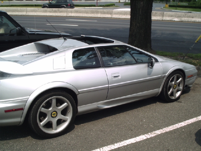 Silver sports car with a rear spoiler, parked on asphalt. A black SUV is partially visible on the left